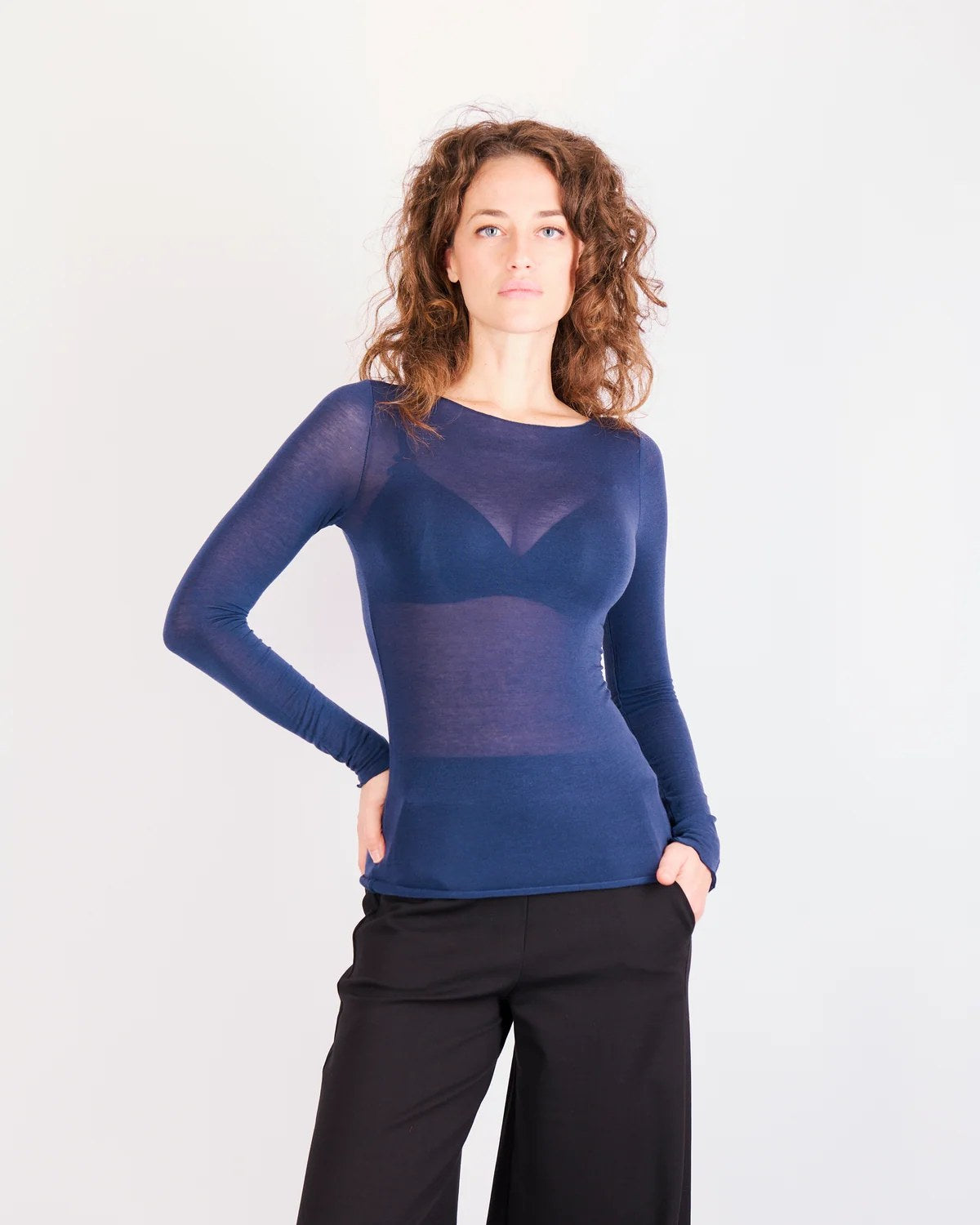 Donna indossa maglia ultraleggera scollo a barchetta blu semitrasparente con pantaloni neri a gamba larga